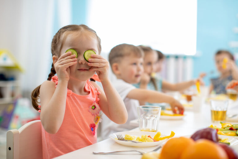Little girl playing with cucumbers at lunch